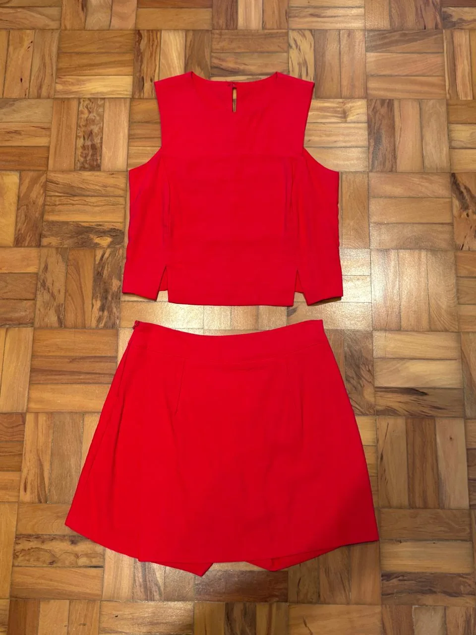Conjunto vermelho de top e saia estendido no chão de taco, foto amadora de celular