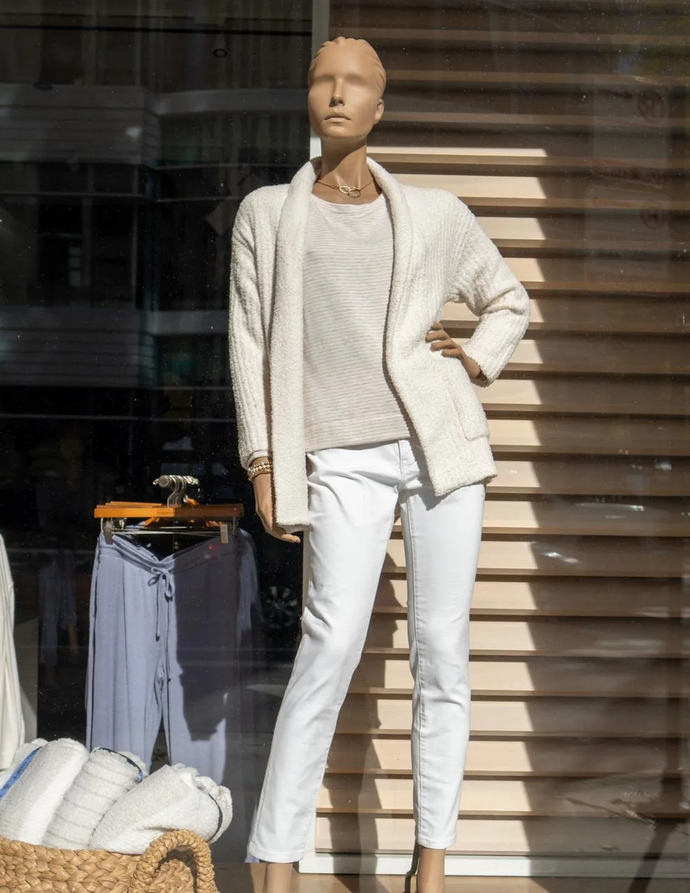 Cardigan off-white, blusa listrada e calça branca num manequim de vitrine
